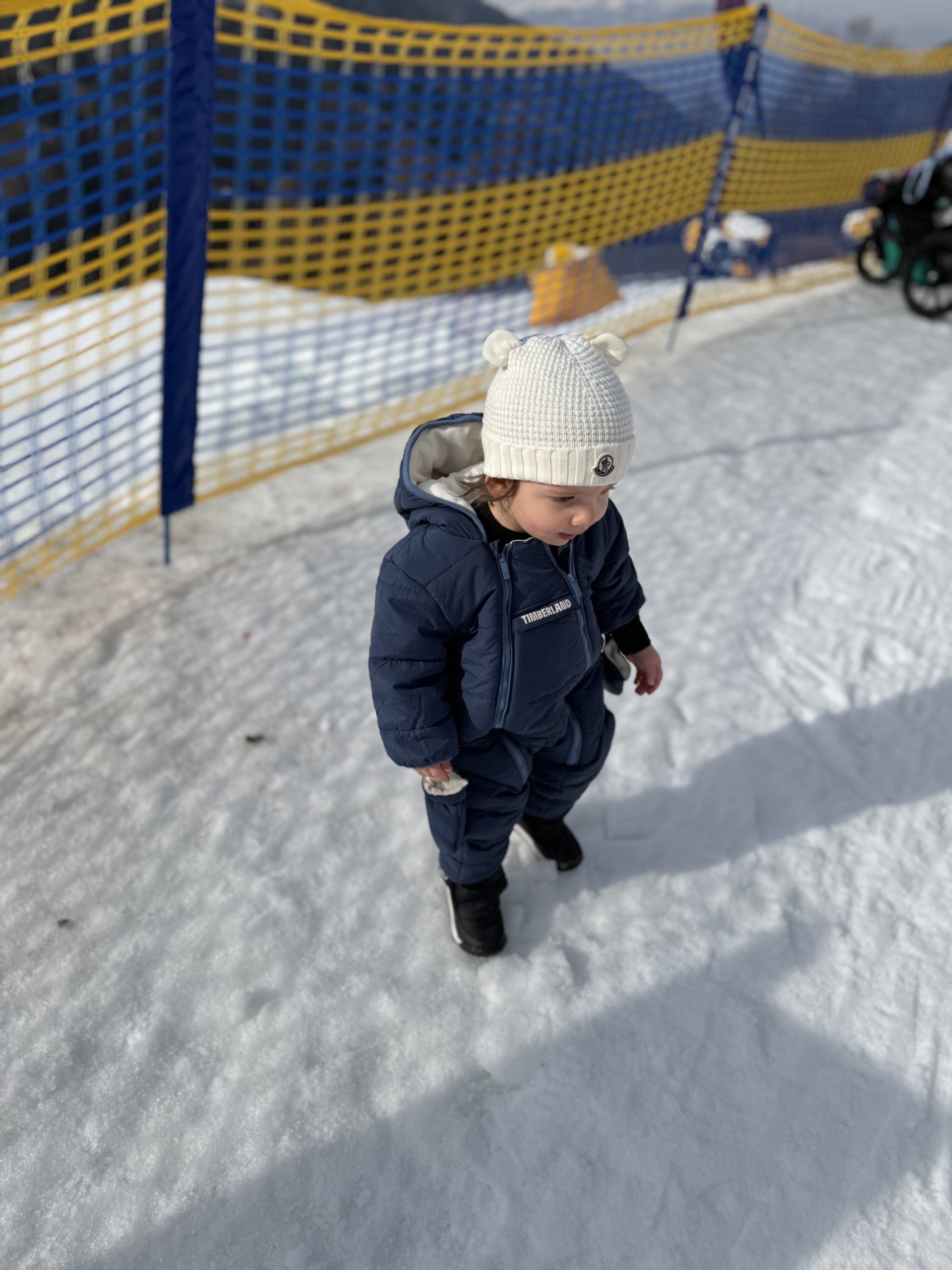 Toddler in the snow wearing a snow suit and cute hat.
